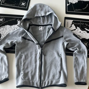 Grå Nike tech  - Snygg grå hoodie från Nike i mycket bra kvalité knappast använd, bara dragkedjan som har blivit lite sliten men det är knappast något man märker.