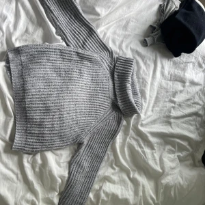 Grå stickad polotröja från Ü - Säljer en chunky grå stickad polotröja från Ü med bred ribbad krage och långa ärmar. Tröjan har en grovstickad struktur och är perfekt för kyliga dagar. Enkel att matcha med jeans eller kjol för en chill look.