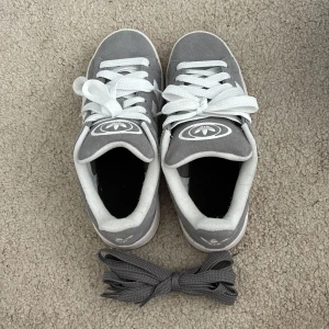 Grå adidas Campus sneakers mocka, pris diskuteras!!! - Snygga grå adidas Campus sneakers i mocka med klassiska vita ränder på sidorna och vit logga på plösen. Skorna har vita snören och extra gråa skosnören medföljer. Låg modell med platt sula och gummisula undertill. Perfekta för en clean och stilren look. Pris diskuteras!!!