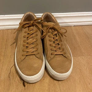 Beiga mockasneakers med vit sula - Snygga sneakers i beige mocka med klassisk låg profil och vit platt gummisula. Skorna har rund tå, snörning och stilren design som passar till det mesta. Obetydligt använda.