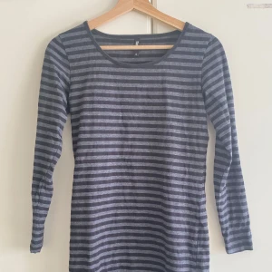 Randig mellanlång klänning i grått - Snygg mellanlång klänning i storlek S. Klänningen har horisontella ränder i mörkgrå och ljusgrå toner, rund halsringning och en smal passform. Perfekt för dig som gillar enkel och stilren design med lite edge.