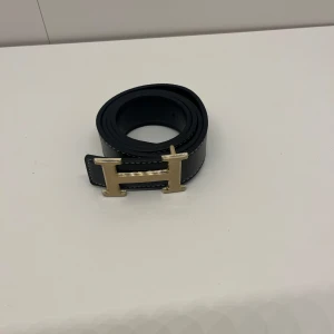 Bälte - Ett svart  bälte med guldig logga i storlek 105 cm och den är helt ny. Pris kan diskuteras och skriv om du har några frågor. 