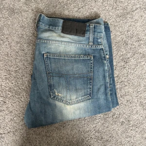 Blå ripped jeans tiger of Sweden 34/32 - Säljer ett par blå jeans från tiger of Sweden i ' med slitna och trasiga detaljer på framsidan. Jeansen har klassisk femficksdesign, normal passform och är tillverkade i bomull. Perfekta för dig som gillar en edgy streetstil.