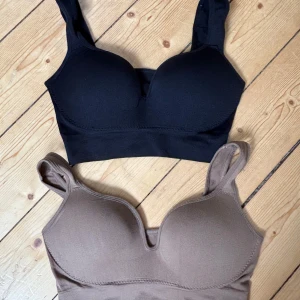 Träningsbhar med push-up - Två sömlösa toppar i sportig stil, en svart och en brun. Båda har breda axelband, vadderade kupor och är tillverkade i stretchigt material för en bekväm passform. Perfekta för träning eller chill dagar.