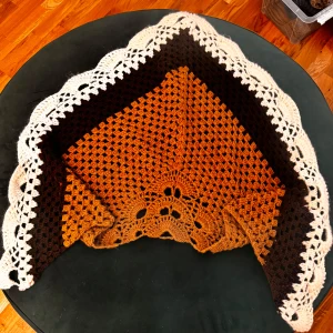 Handvirkad trekantig halsduk i brunt - Unik handvirkad halsduk i trekantig form med breda ränder i brunt, beige och mörkbrunt. Snyggt hålmönster och vågig kant i beige ger extra detalj. Perfekt att svepa runt axlarna för en chill och kreativ look. Materialet är mjukt och stickat, passar dig som gillar retro och boho.