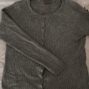 Grå kofta från Vero Moda - Säljer en grå kofta från Vero Moda i storlek S. Koftan har ett snyggt stickat mönster, rund halsringning och knäppning framtill med flera knappar. Perfekt att slänga på sig över en t-shirt eller linne när det är lite kyligt. Har den även i marinblå, den ligger ute i en egen annons!
