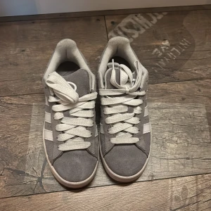 Adidas Campus grå sneakers mocka - Säljer ett par Adidas Campus sneakers i grå mocka med vita detaljer och klassiska tre ränder på sidorna. Knappt använda, storlek 36/37