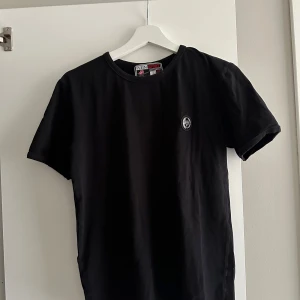 Svart t-shirt från Plein Sport - Svart t-shirt från Plein Sport med rund hals och korta ärmar. Diskret logotyp-patch på bröstet. Bra skick. Anledning till försäljning är att den är för liten för mig 