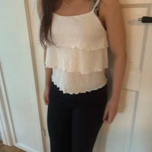 Vit volang-linnetopp med tunna band - Supersöt vit linnetopp med tunna axelband och flera lager volanger. Toppen är ärmlös och har en lätt, luftig känsla som passar perfekt till varma dagar. Stilren och enkel att matcha med både jeans och kjol.🩷❤️