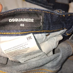 DSQUARED2 blå jeans  - Säljer ett par blå jeans från DSQUARED2 i storlek 48. Jeansen har coola slitningar, färgstänk och en tvättad look. Klassisk femficksmodell med smal passform och snygga detaljer. Perfekta för dig som gillar streetstyle och vill sticka ut.
