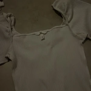 Vit ribbad tröja från H&M - Säljer en söt vit ribbad tröjafrån H&M med puffärmar och fyrkantig ringning. Tröjan har en lätt stretchig känsla och är perfekt för att styla med jeans eller kjol. Enkel och stilren design som passar till många tillfällen.