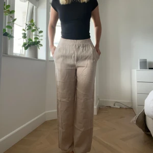 Beiga linnebyxor med resårmidja - Säljer ett par beiga linnebyxor med avslappnad passform och resår i midjan. Byxorna har raka, vida ben och sidfickor. Använd fåtal gånger, fint skick