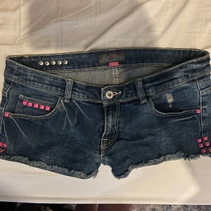 Mörkblå jeansshorts med rosa nitar - Unika jeansshorts med rosa nitar och låg midja. Se bild 3 för midjemått. Shortsen är i mycket bra skick. Se sista 2 bilderna för bättre ljus.