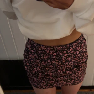 Svart minikjol med rosa blommor från H&M - Säljer en svart kortkjol från H&M med tätt blommigt mönster i rosa. Kjolen har en tight passform och är tillverkad i polyester. Perfekt för dig som gillar en feminin och trendig stil.