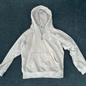 Beige hoodie med halv dragkedja från Harlaut apparel  - Säljer en beige hoodie från Harlaut har blivit använd en gång med halv dragkedja och känguruficka framtill. Tröjan har huva med snörning och långa ärmar. Perfekt för en avslappnad stil.
