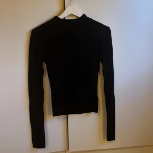 Svart ribbad tröja - Snygg svart ribbad tröja med lång ärm och hög hals. Perfekt för en stilren look. Passar bra till både jeans och kjol. Använd ett fåtal gånger
