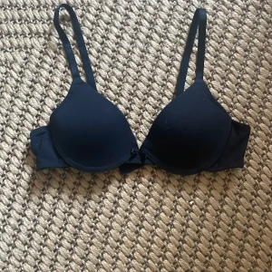 Svart bh med justerbara axelband - Säljer en stilren svart bh med jjusterbara axelband och vadderade kupor. Perfekt för vardagsbruk och ger bra stöd. Den har en klassisk design med hakknäppning bak.