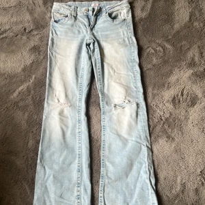 Ljusblå Low waist bootcut jeans  - Ljusblå Low waist jeans från Gina Tricot med bootcut passform och slitningar vid knäna. Klassisk femficksmodell med knapp och dragkedja framtill. Perfekta för dig som gillar en trendig stil!
