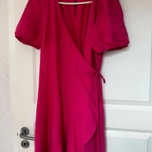 Ceriserosa omlottklänning från Bondelid - Säljer en ceriserosa omlottklänning från Bondelid med puffärmar och knyt i midjan. Klänningen har korta ärmar och en feminin v-ringning. Perfekt för sommarens alla tillfällen!