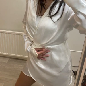 Vit klänning från Zara - Elegant vit omlottklänning i satin med långa ärmar och knytning i midjan. Perfekt för en stilren look!!🤍🤍