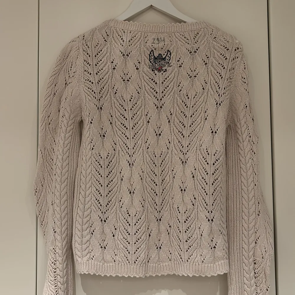 Supersnygg beige stickad tröja från Odd Molly med hålmönster och rund hals. Tröjan har långa ärmar och fina detaljer, inklusive broderad logga på ryggen. Perfekt för lager-på-lager och en mysig stil.. Neuleet.