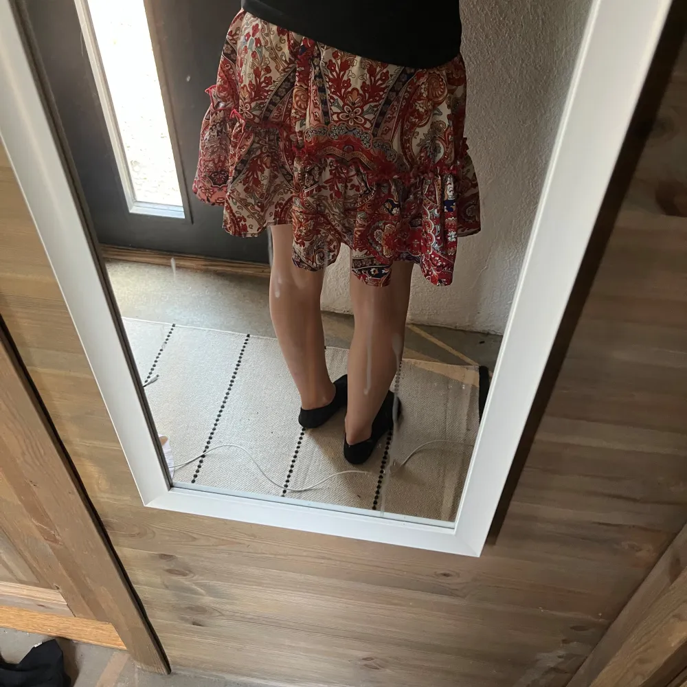 Kort kjol från SHEIN med färgstarkt paisleymönster i rött, blått och beige. Kjolen har volangdetaljer och resår i midjan för en bekväm passform. Tillverkad i polyester med lite stretch.. Hameet.