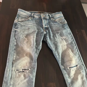 Blå slitna jeansbyxor från Jack and Jones  - Säljer ett par blå jeansbyxor från Jack and Jones med slitningar och trasiga detaljer. Storlek 31 30