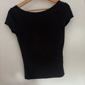 mörkgrå topp med djup rygg - Säljer en mörkgrå topp med korta ärmar och en djup, rundad rygg. Enkel och stilren design som passar perfekt till många olika outfits. Mjuk och stretchig känsla.