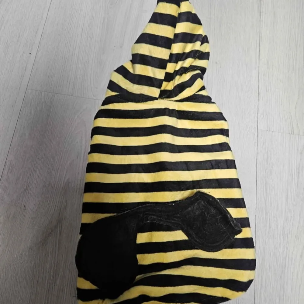 Gul och svart randig jacka med huva för hunden och dekorativt svart märke på ryggen. Jackan är tillverkad i mjuk polyester och har öppningar för framben. Perfekt för dig som vill sticka ut med en färgglad och lekfull look.. Muu.