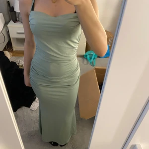 Klänning - Säljer en elegant ljusgrön långklänning med smala axelband och figurnära passform. Klänningen har draperade detaljer vid midjan och en mjukt rundad urringning. Perfekt för speciella tillfällen! Storlek xs och är som ny