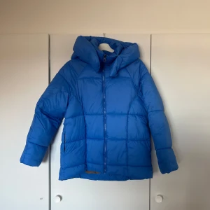 Blå pufferjacka med huva - Säljer en blå pufferjacka med stor huva och dragkedja framtill. Jackan har quiltad design och två fickor på sidorna. Perfekt för kyliga dagar och enkel att styla till olika outfits. Den är helt ny och lappen sitter fortfarande kvar, nytt pris är 600kr🫧🩷