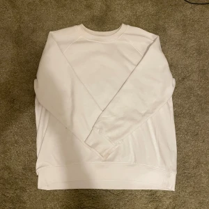 Vit sweatshirt från H&M - En basic vit sweatshirt från H&M i mjuk bomullsmix. Tröjan har rund halsringning, långa ärmar och ribbade muddar vid ärmslut och nederkant. Perfekt för en clean och enkel stil.