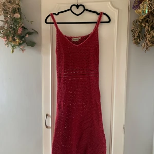 Röd stickad klänning från Indiska - Snygg röd stickad klänning från Indiska med smala axelband och v-ringning. Perfekt för sommarens varma dagar. Klänningen har ett dekorativt hålmönster och en avslappnad passform.