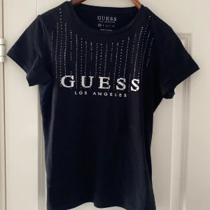 Svart t-shirt från Guess - Fin svart t-shirt från Guess med glittrande strassdetaljer och stor logga framtill.  Storlek xs men passar även s.                                                           Mycket bra skick. 