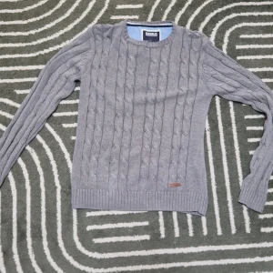 Grå stickad tröja från Bondelid - Säljer en stilren grå stickad tröja från Bondelid med klassiskt flätmönster. Tröjan har långa ärmar och en rund halsringning. Perfekt för kyligare dagar. 🧶