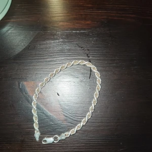 Silverfärgat armband med tvinnad design - Snyggt silverfärgat armband med en elegant tvinnad design. Perfekt för att ge en stilren touch till din outfit. Armbandet har en praktisk låsning som gör det enkelt att ta på och av. Cordell