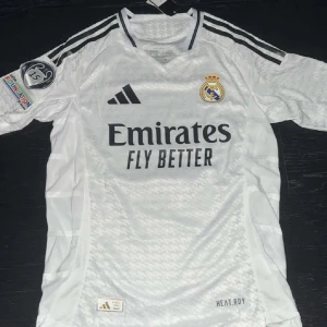 Vit Real Madrid fotbollströja, Mbappe 9 - Snygg vit Real Madrid fotbollströja från Adidas med Mbappé och nummer 9 på ryggen. Tröjan är player version, och har UCL badge på ärmen. Tröjan är helt ny och oanvänd.
