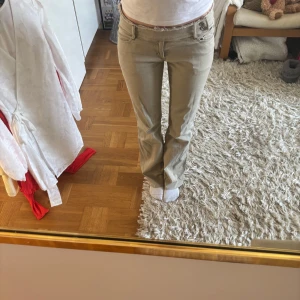 Beige byxor med knappar - Snygga beige byxor med låg midja och bootcut-stil. Byxorna har dekorativa knappar och fickor både fram och bak. Perfekta för en avslappnad look.