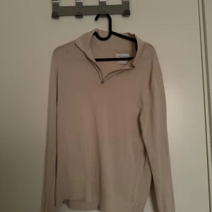 Beige tröja med dragkedja från These Glory Days - Säljer en stilren beige tröja från These Glory Days i mjuk bomull. Tröjan har halv dragkedja vid halsen och långa ärmar. Perfekt för lager-på-lager och enkel att matcha med olika outfits.