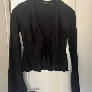 Svart ribbad topp - Säljer en svart ribbad topp från Gina Tricot med långa ärmar och knytning framtill. Toppen har en v-ringad design. Jätte bra skick💕💕