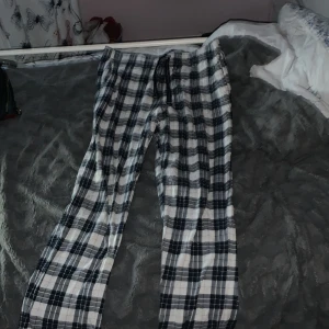 Rutiga mjukisbyxor med snörning - Säljer ett par sköna mjukisbyxor i svartvitt rutigt mönster. Byxorna har dragsko i midjan för perfekt passform och är tillverkade i mjukt bomullstyg. Perfekta för chill dagar hemma eller när du vill vara extra bekväm.