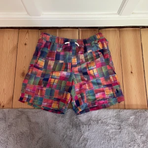 Färgglada rutiga shorts Polo Ralph Lauren - Säljer ett par färgglada rutiga shorts från Polo Ralph Lauren. De har elastisk midja med snörning och bakficka med knapp. Mönstret är en mix av rött, blått, grönt, gult och rosa. Perfekta för sommaren och riktigt sköna att ha på sig.