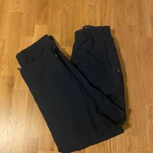 Mörkblå täckbyxor från CCM - Mörkblå täckbyxor från CCM med elastisk midja och dragkedjor vid fickorna. Perfekta för vintern och sportiga aktiviteter. Snygg och enkel design som funkar när du vill hålla dig varm ute.
