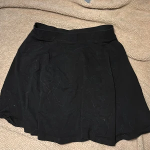 Svart kortkjol från H&M - Enkel och stilren svart kortkjol från H&M med bred midja. Kjolen har en lätt utsvängd form och är perfekt för dig som gillar en klassisk look. Passar till många olika stilar och är lätt att matcha med både sneakers och boots.ENDAST ANDVÄND EN GÅNG 