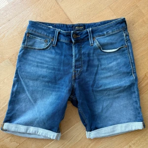 Blå jeansshorts från Jack & Jones - Snygga blå jeansshorts från Jack & Jones i regular fit. Klassisk femficksmodell med uppvikta benslut och detaljerade sömmar. Perfekta för sommaren och lätta att matcha med t-shirt eller hoodie. Skön passform och tidlös stil.