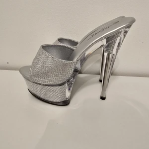Silverfärgade platåpumps med hög klack - Glittriga silverpumps med öppen tå, platåsula och riktigt hög klack. Skorna har ett mönstrat tyg med små cirklar och en cool transparent detalj i sulan. Perfekta för dig som vill sticka ut och älskar metallic vibes.