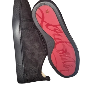 Svarta sneakers från Christian Louboutin - Snygga svarta sneakers från Christian Louboutin i mocka med klassisk röd sula och diskret logga. Skorna har rund tå, svarta snören och stilren design som sticker ut med exklusiv känsla. Perfekta för dig som vill ha något unikt och lyxigt.