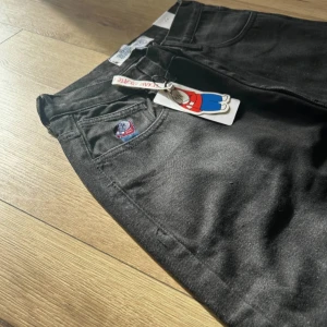 Svarta jeans från Polar Skate Co - Svarta jeans från Polar Skate Co med broderad logga vid fickan och klassisk femficksdesign. Jeansen har en rak passform och är tillverkade i kraftig bomullsdenim. Perfekta för dig som gillar streetwear och vill ha en clean look.