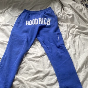 Blåa mjukisbyxor från Hoodrich - Blåa mjukisbyxor från Hoodrich med vit broderad logga framtill. Byxorna har elastisk midja, sidofickor och en extra ficka på benet. Tillverkade i mjukt bomullsmaterial för maximal komfort och streetkänsla. Tyvärr har den ju fått tre små fläckar som knappt syns vid användning men det går nog bort i tvätten om man använder vanish.