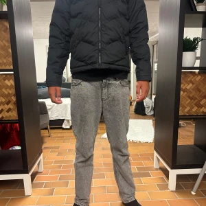 Svart pufferjacka från Nike - Svart pufferjacka från Nike med klassisk logga på insidan. Jackan har lång ärm, dragkedja framtill och är vadderad för extra värme. Snygg, enkel design med diskreta detaljer och passar perfekt när det är kallt ute.